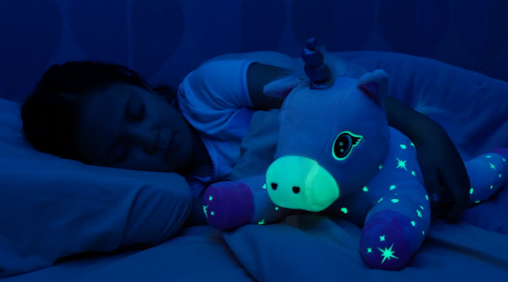 A girl in bed asleep hugging Glimmer the Glowing Unicorn and Glimmer is glowing in the dark